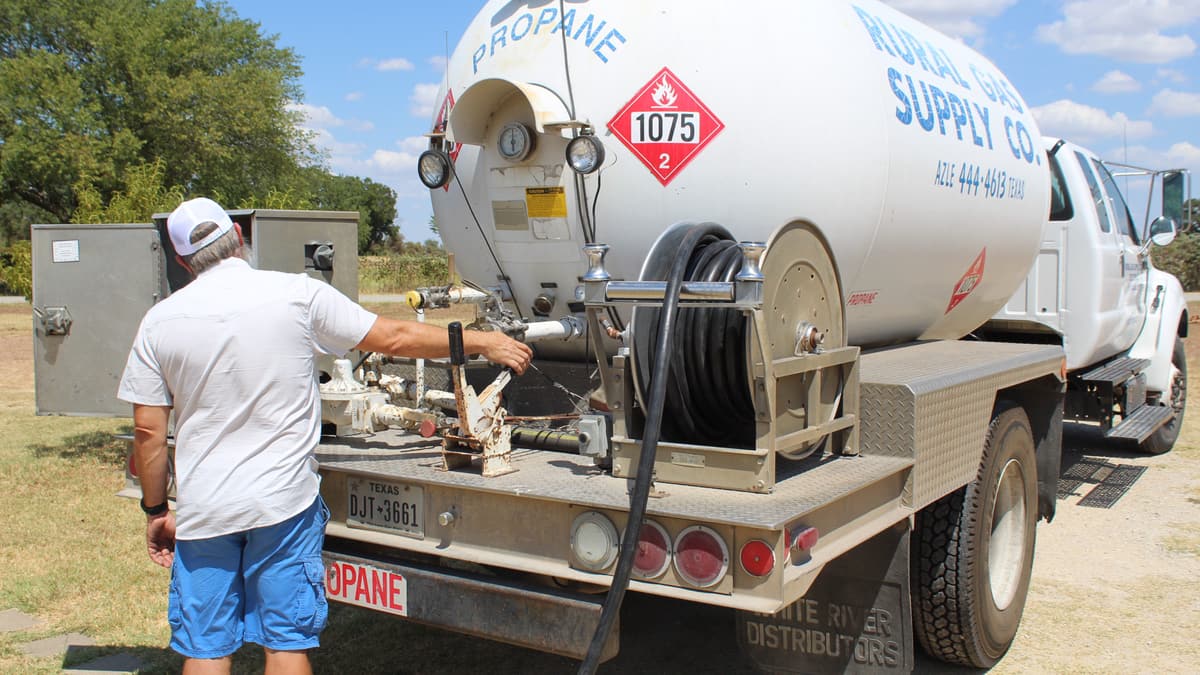 Rural Gas Supply bobtail truck parked in the grass yard, the UN1075 propane placard and hose reel visible on the rear deck.