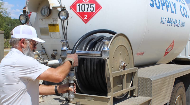 A Rural Gas Supply crew member coupling the delivery hose at the reel on the back of the service truck.